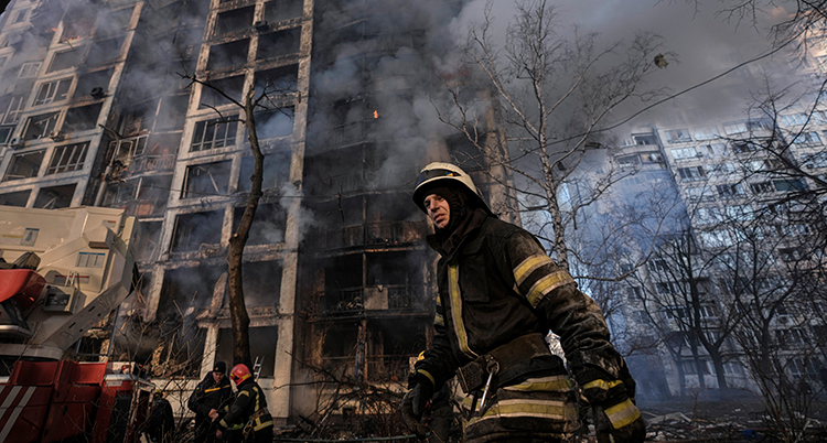 En brandman framför ett bombat hus. Det ryker i bakgrunden
