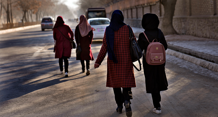 flickor med ryggsäckar går på en gata i Afghanistan.