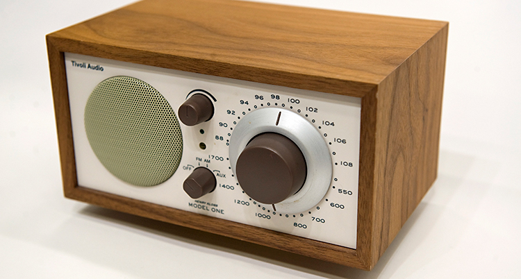 En radio som står på ett bord. Radion har en ram av trä. Radion har olika knappar och rattar.