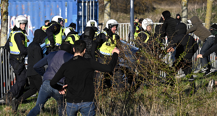 Svartklädda unga män ser ut att attackera poliser i skyddskläder.