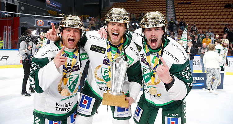 Tre ishockeyspelare står på isen och jublar. De har guldhjälmar på sig.