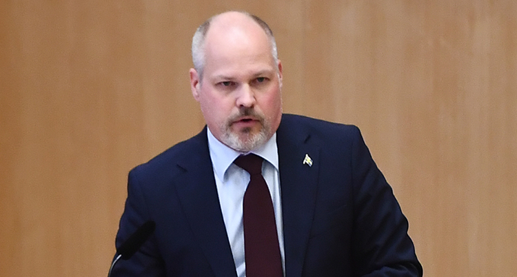 Morgan Johansson står i riksdagen och pratar. Han har kostym och slips.