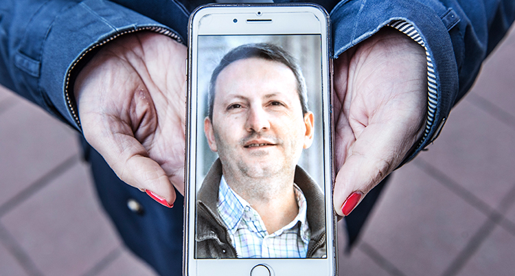 Två händer håller i en mobil. i mobilen syns en bild på en man.