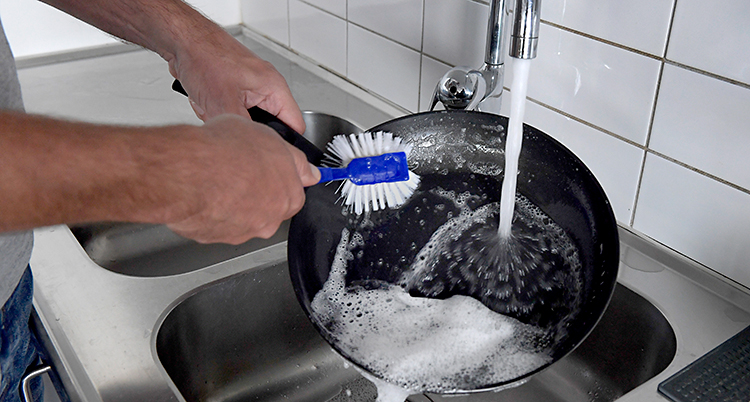 En person står och diskar en stekpanna under kranen.