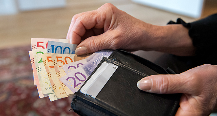 En närbild på två gamla händer som håller i en plånbok med sedlar.