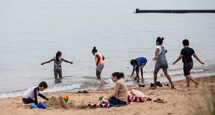 Flera barn går ned i vattnet från stranden. Ett par barn sitter på stranden och gräver i sanden.