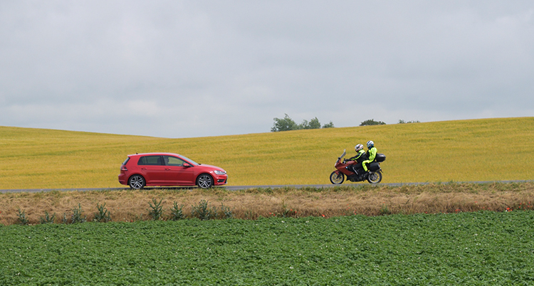 En bil och en motorcykel framför ett rapsfält.