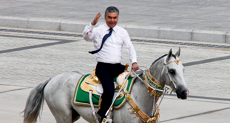 En man i slips och vid skjorta rider på en häst och vinkar.