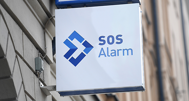 En skylt sitter på ett hus. På skylten står det SOS Alarm.