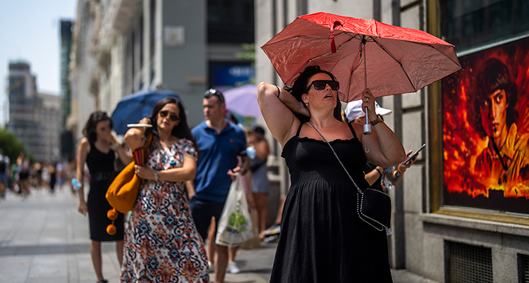 Personer går på en gata i Madrid. Kvinnan närmast kameran har ett rött paraply.