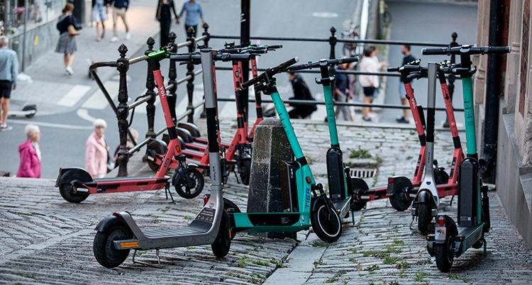 Rosa och turkosa elsparkcyklar står parkerade på en kullerstensgatan.