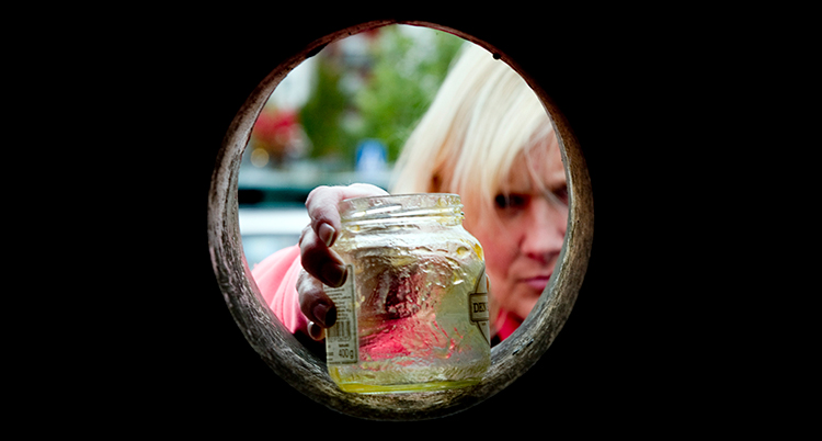 Kvinna lägger en glasburk i ett återvinningskärl.