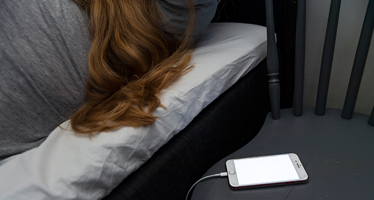 En kvinna i en säng med en mobil på sängbordet.