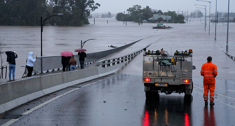 EN bil och människor står på en väg som framför dem är helt översvämmad.