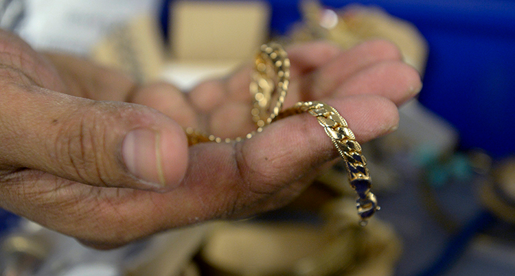 En gammal hand håller i ett guldsmycke.