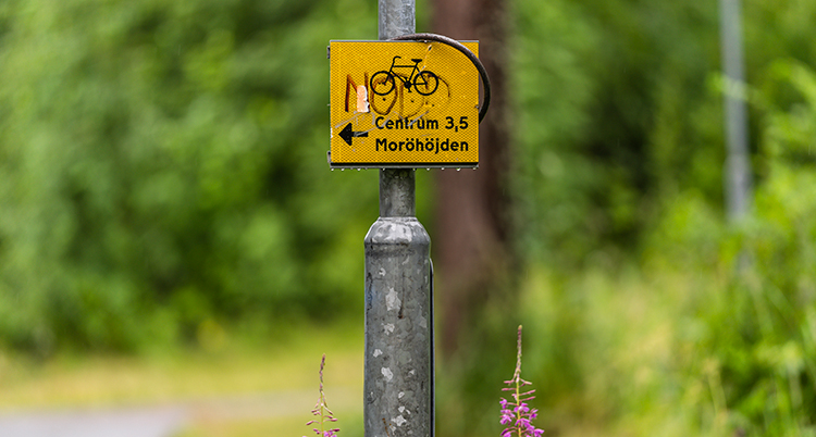 En gul skylt med en bild på en cykel sitter på en träpelare.