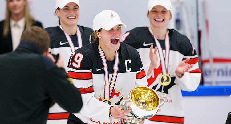 Glada kvinnliga ishockeyspelare från Kanada med segerbucklan.