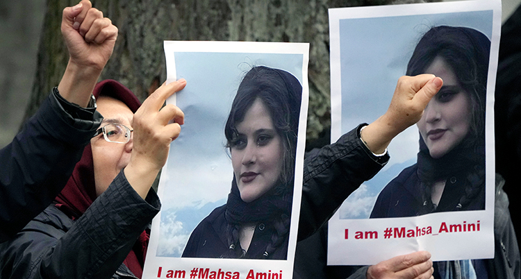 En knuten näve och två andra händer håller upp bilder på Mahsa Amini.
