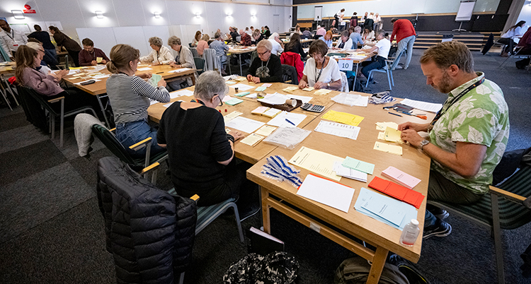 Människor sitter vid ett bord fullt med valsedlar.