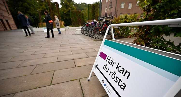 En skult står på trottoaren i förgrunden. Länge bort ses människor som väntar.