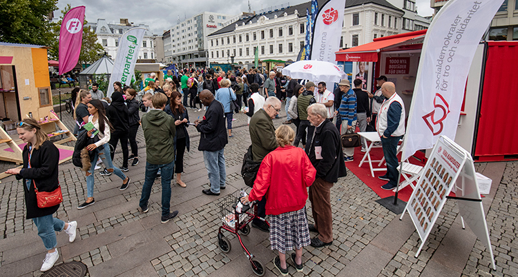 Människor på ett torg. Partiernas valbodar runt torget.