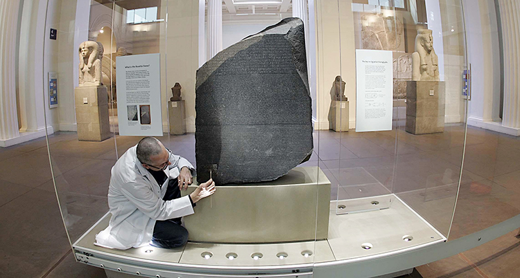 En man som jobbar på museet sitter och tittar på stenen.