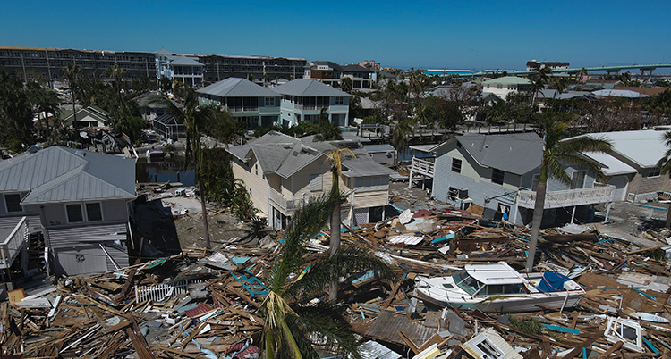 Bild tagen ovanifrån på ett området med hus som blivit helt förstörda. En båt ligger också på marken vid allt bråte.
