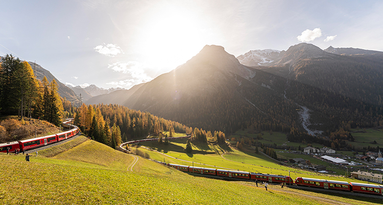 Solen skiner över ett landskap i Alperna. Ett tåg kör fram.