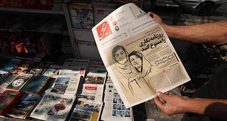 En man håller upp en tidning. På framsidan av tidningen är det en teckning som visar två kvinnor.