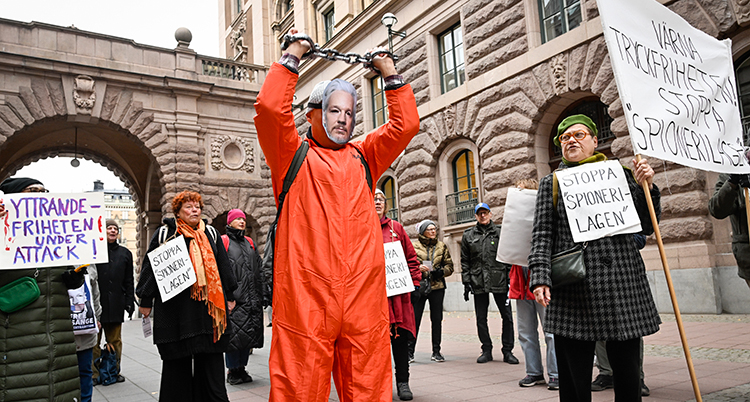 De håller upp skyltar. En man har på sig en orange dräkt och en mask.