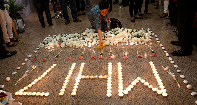 Ljus står i rad och bildar ordet MH17. En kvinna tänder ett ljus.
