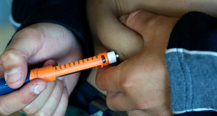 En person tar en spruta med insulin i magen.
