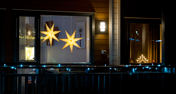 Julstjärnor och ljusstakar lyser i fönstren på ett hus.