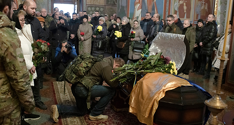 En begravning i ett kloster. Människor står runt en kista.