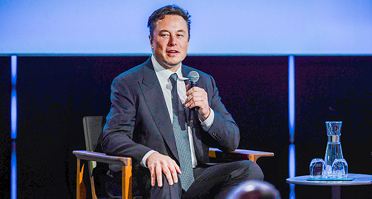 Elon Musk sitter på en stol på en scen och pratar i en mikrofon.