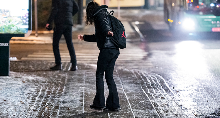 En kvinna med svarta kläder går på en isig trottoar och halkar