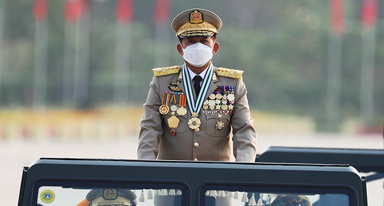 En militär i uniform och munskydd står i en bil