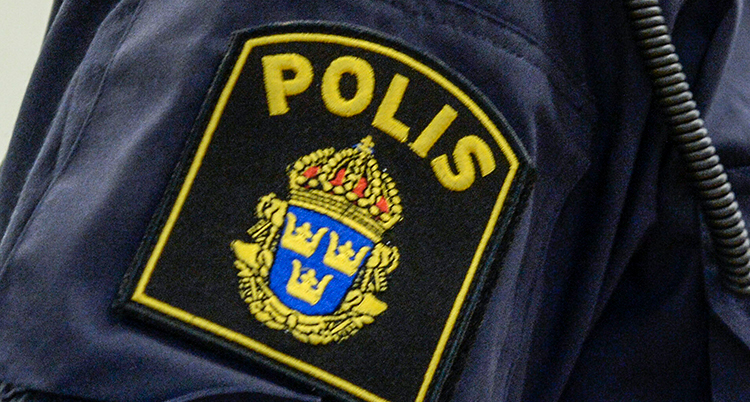 En närbild på en polis ärm på en uniform. Ett märke där det står polis.