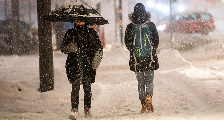Två personer går i en snöig stad. En person har ett paraply uppfällt.