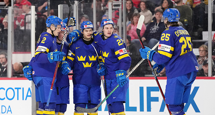 Flera svenska spelare i blå dräkter, blå hjälmar och klubbor är på isen. Publiken syns bakom.