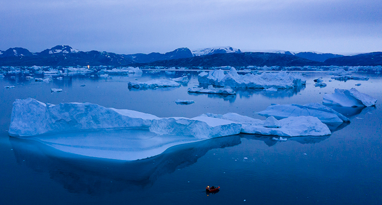 En liten båt syns i vattnet i förgrunden. Bakom syns massor av is och en blålila himmel