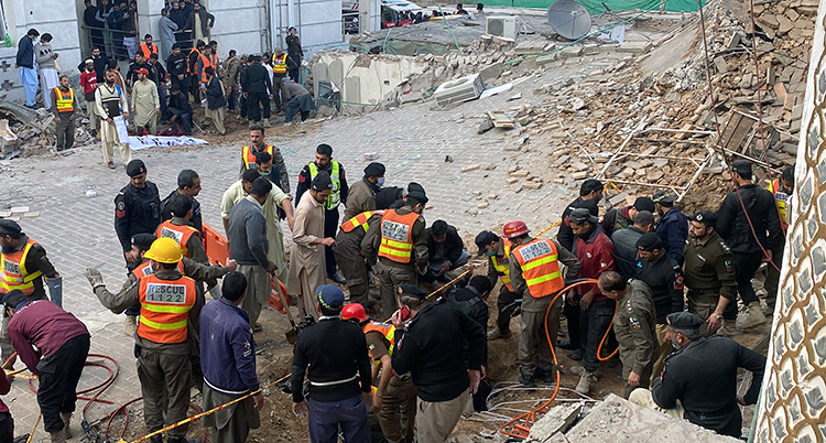 Människor och räddningsarbetare jobbar på något som ser ut som en byggarbetsplats. Bråte överallt.