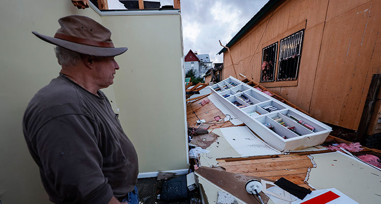 En man i profil. Han tittar på ett förstört hus.