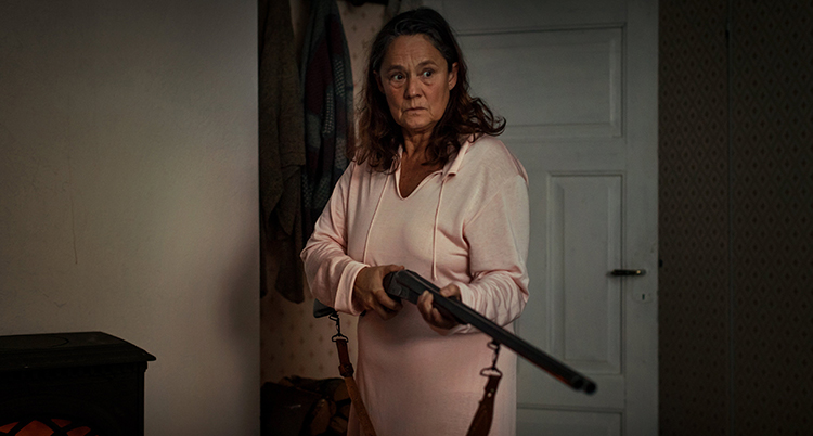 En bild från serien. Pernilla August står med ett gevär i handen.