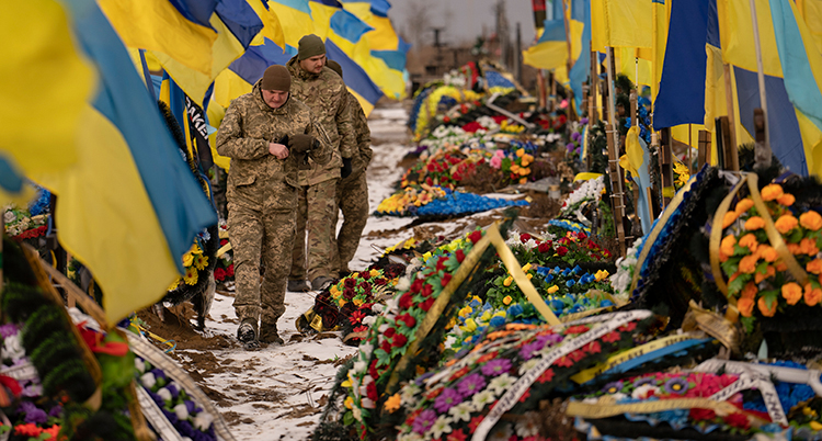 Mycket blommor ligger på gravarna. Två soldater syns i bild.