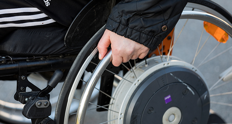 En hand håller om hjulet på en rullstol.