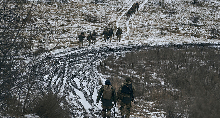 Några soldatklädda män går på en lerig och frusen väg.