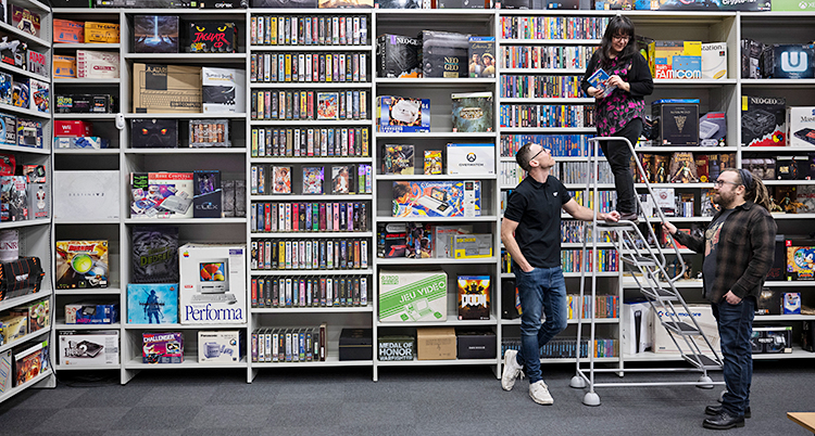Tre personer står vid en hylla som är full av tv-spel och dataspel.