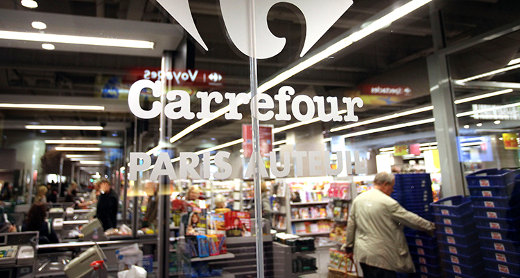 Människor handlar i en mataffär. De syns genom en glasruta där det står Carrefour.