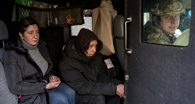 En kvinna och en pojke sitter i en buss. Framför sitter en soldatklädd man och tittar bakåt.